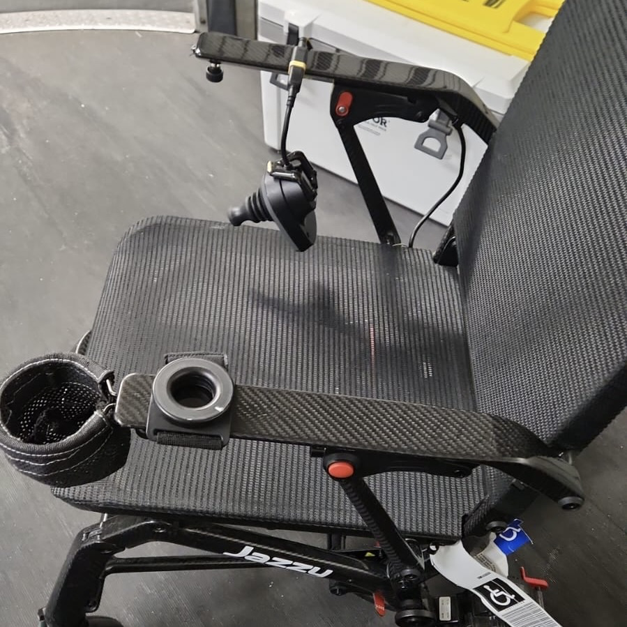 A power wheelchair with a broken joystick at the airport gate.