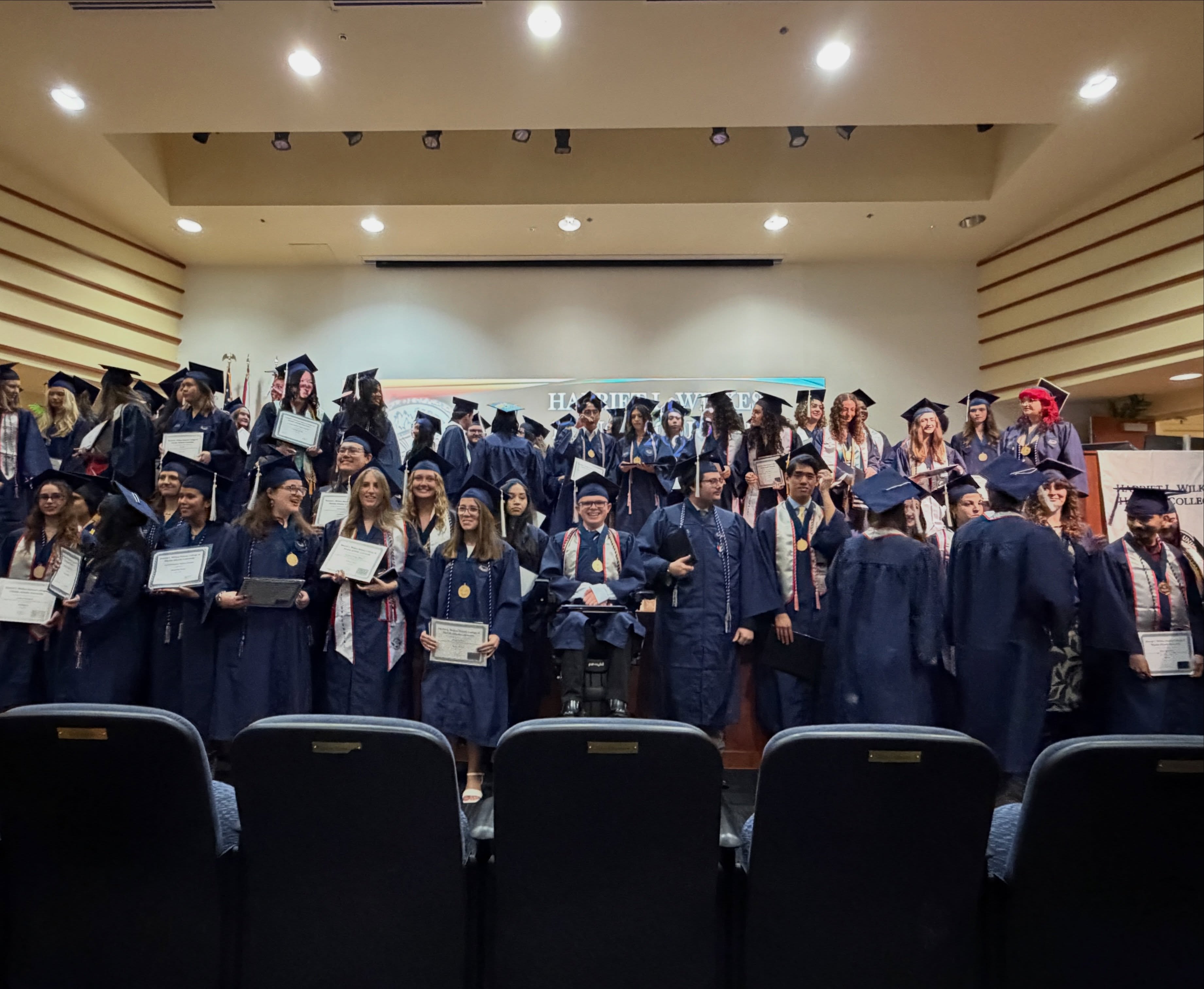 The full Wilkes Honors College Class of 2026 posed across the stage with their certificates, Ryleigh Newman seated in his power wheelchair near the center.