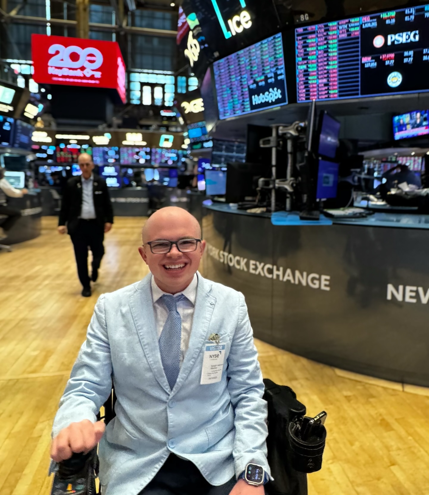 Ryleigh Newman seated beneath the carved 'New York Stock Exchange' marble wall and the brass closing bell.