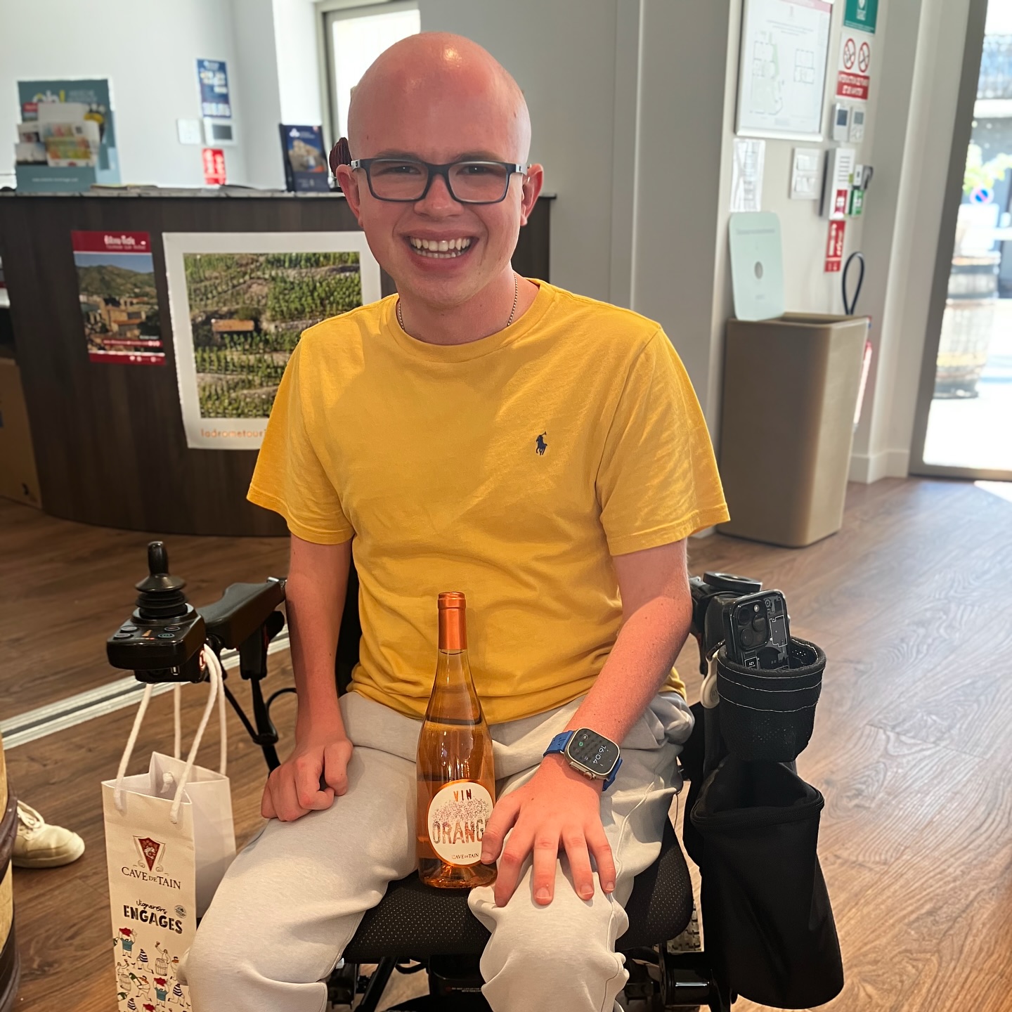 Ryleigh Newman in his wheelchair holding a bottle of orange wine given to him as a birthday gift in the Cave de Tain tasting room.