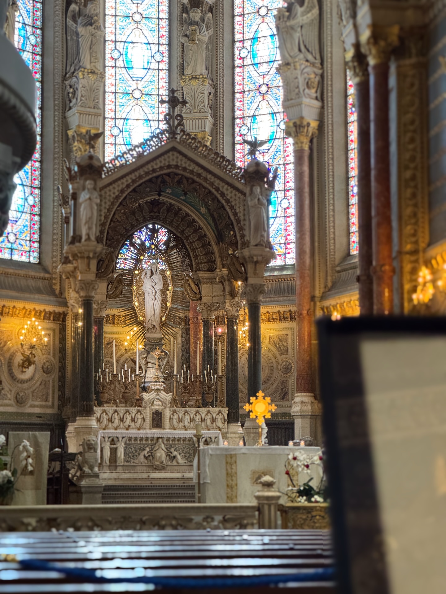 The gilded high altar of the Fourviere basilica glowing beneath tall stained glass windows in Lyon.